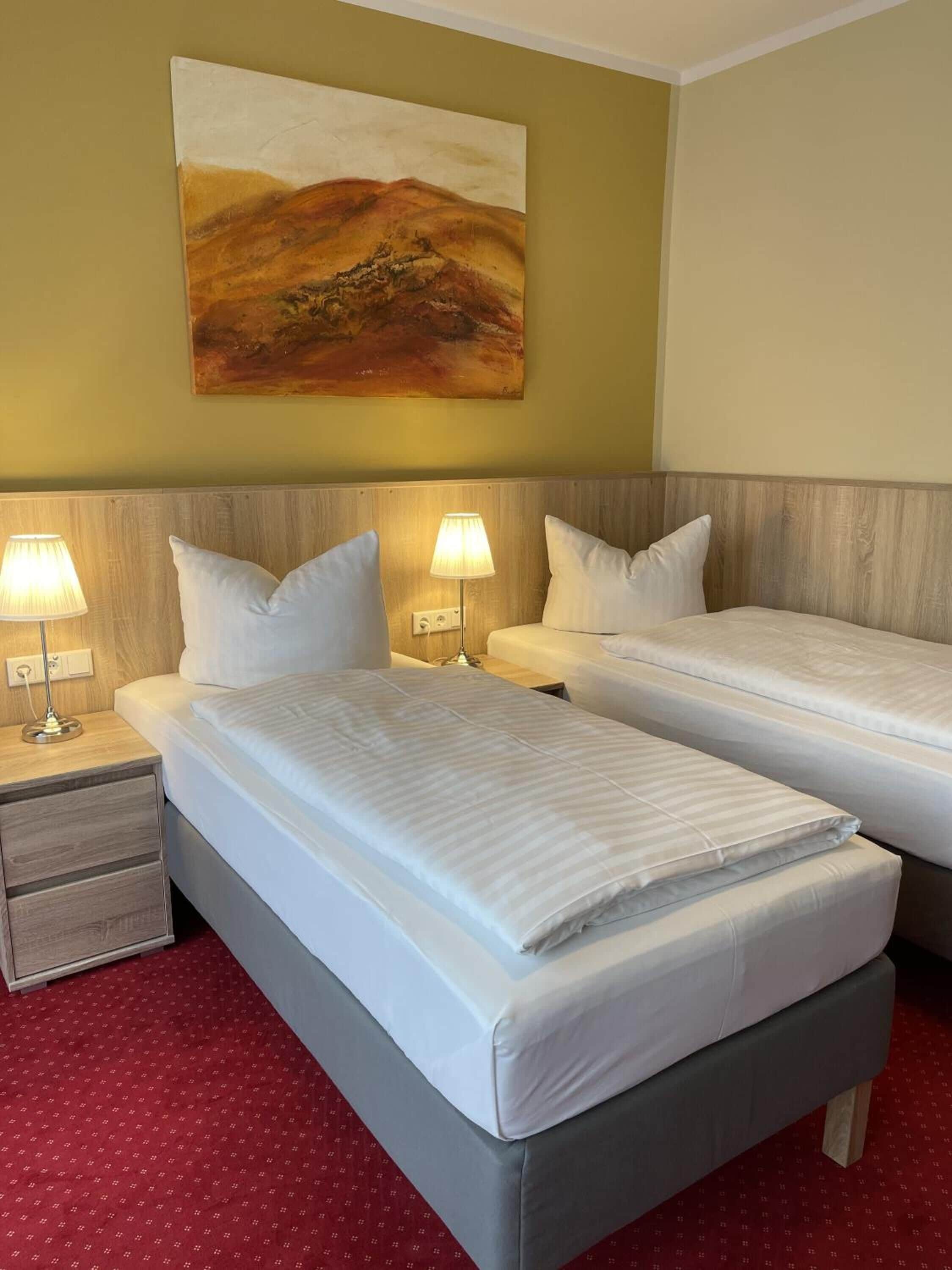 Ein Hotelzimmer mit zwei Betten, einem Nachttisch, einer Lampe und einem Gemälde an der Wand.