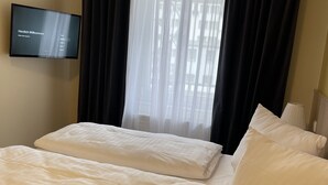 Habitación de hotel con dos camas, un televisor en la pared y un ventanal con cortinas blanco y negro.