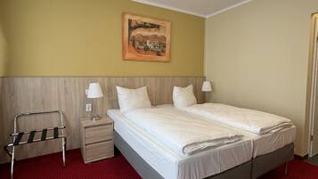 A hotel room with a bed, bedside tables, a lamp, a painting on the wall, and a red carpet.