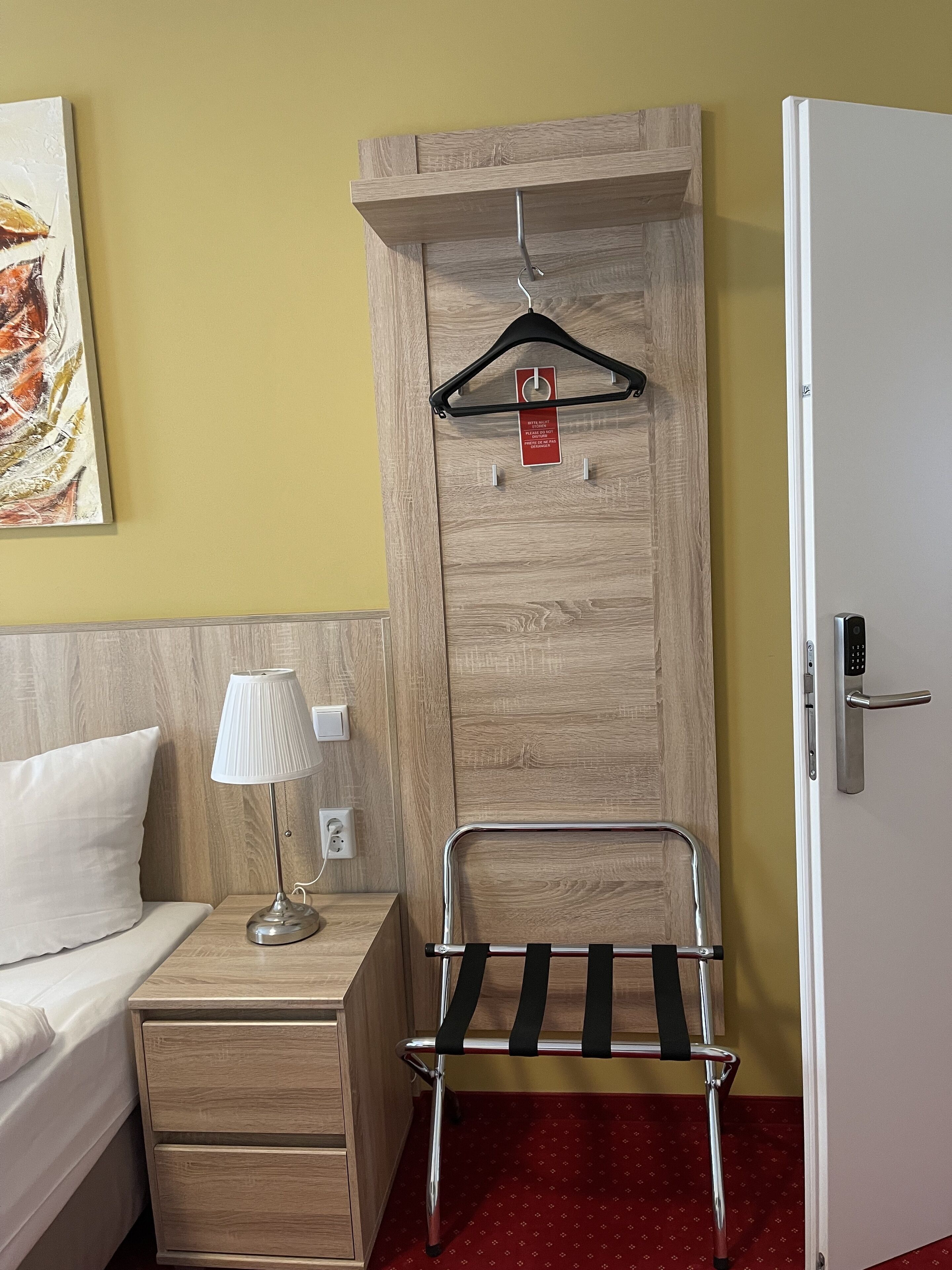 Habitación de hotel con cama, lámpara de noche, armario de madera y una silla metálica con respaldo.