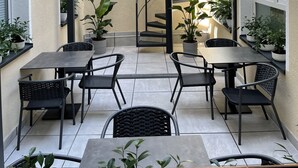 Un espacio al aire libre cubierto con mesas y sillas, una escalera en espiral y plantas en macetas.
