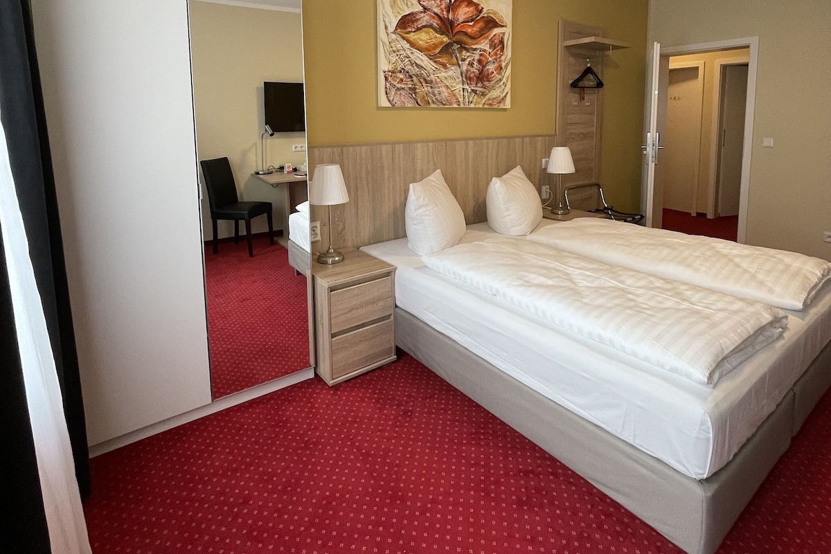 Une chambre d’hôtel comprenant un lit, des tables de chevet, un bureau avec une chaise, un miroir et un tableau au mur.