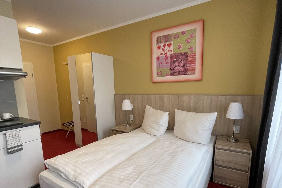 Une chambre d’hôtel avec un grand lit, deux tables de chevet avec des lampes, une armoire, un bureau avec un téléphone et un tableau au mur.
