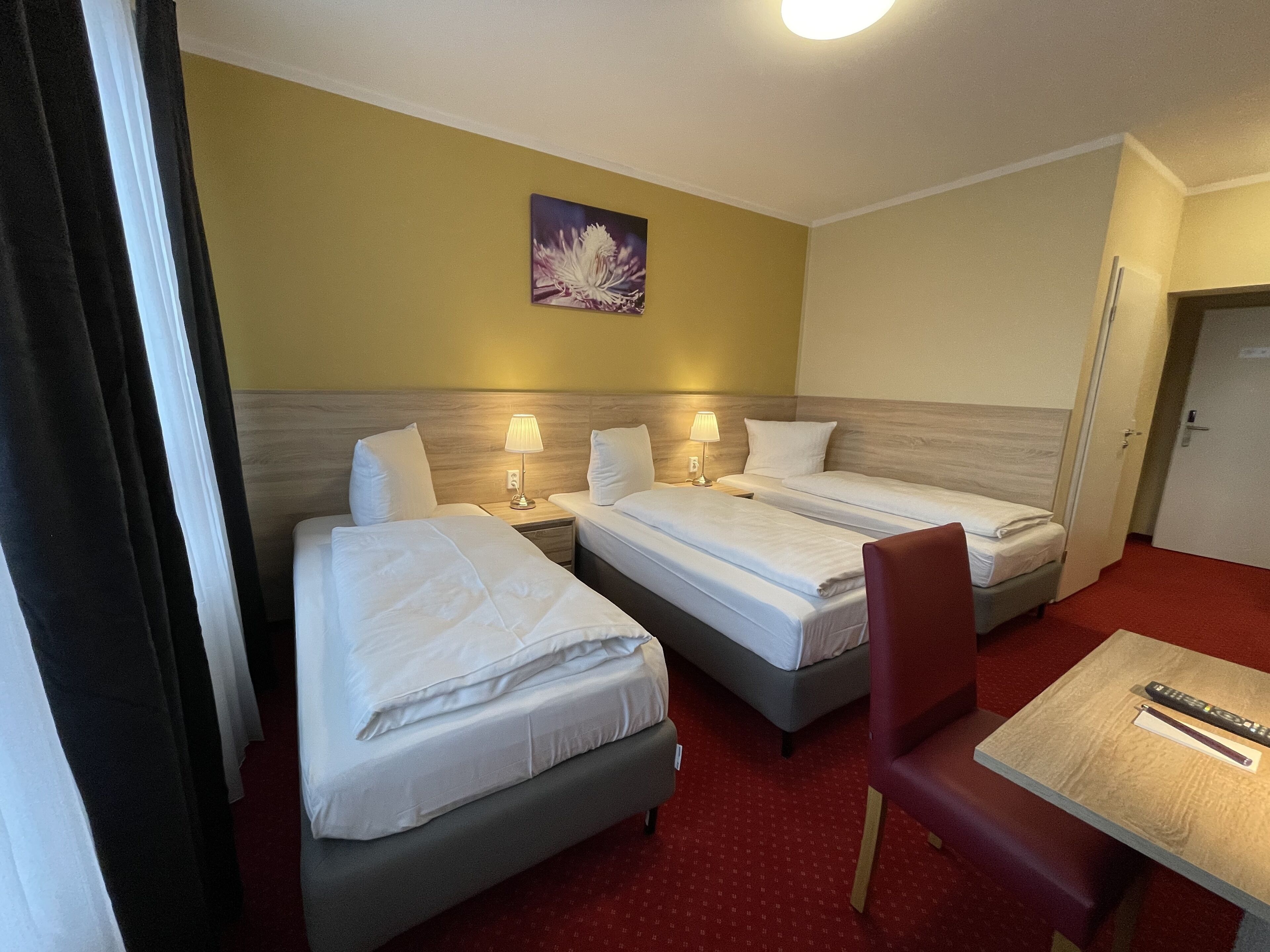 A hotel room with two beds, a small table, and a painting on the wall.