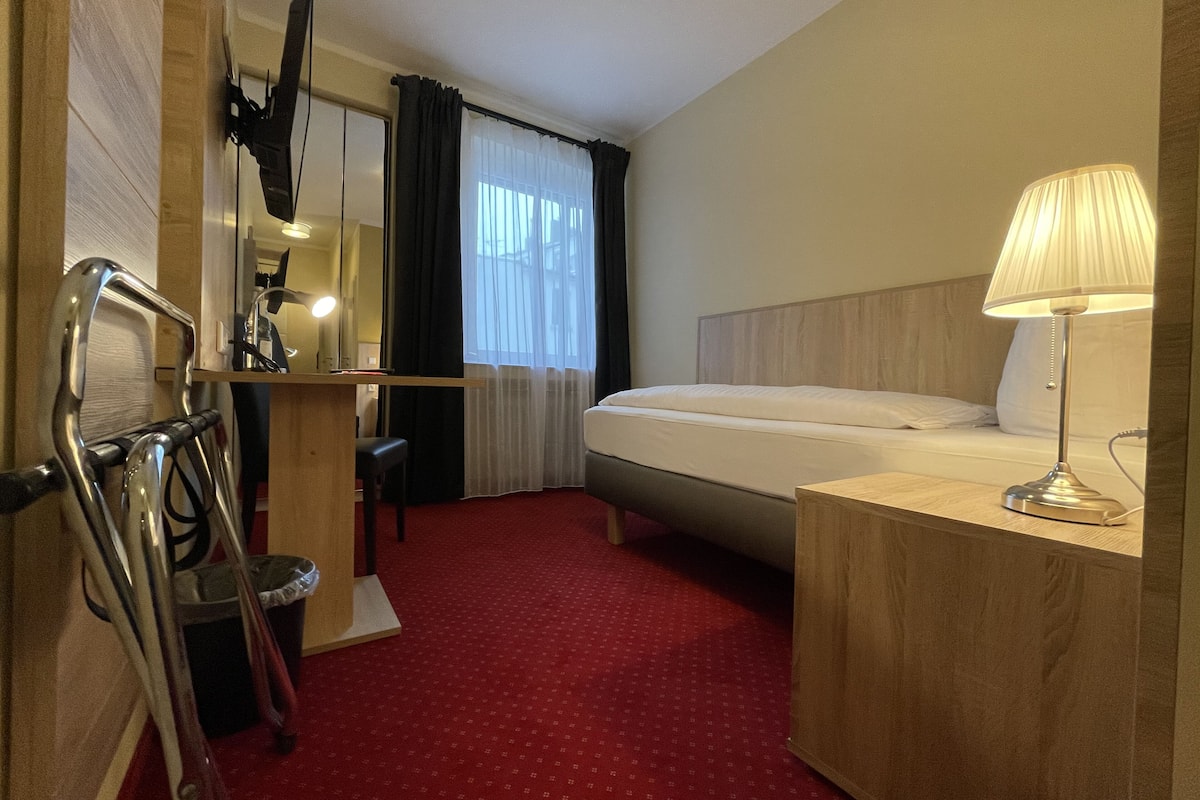 Une chambre d’hôtel avec un lit, un bureau avec une chaise, une lampe et un miroir.