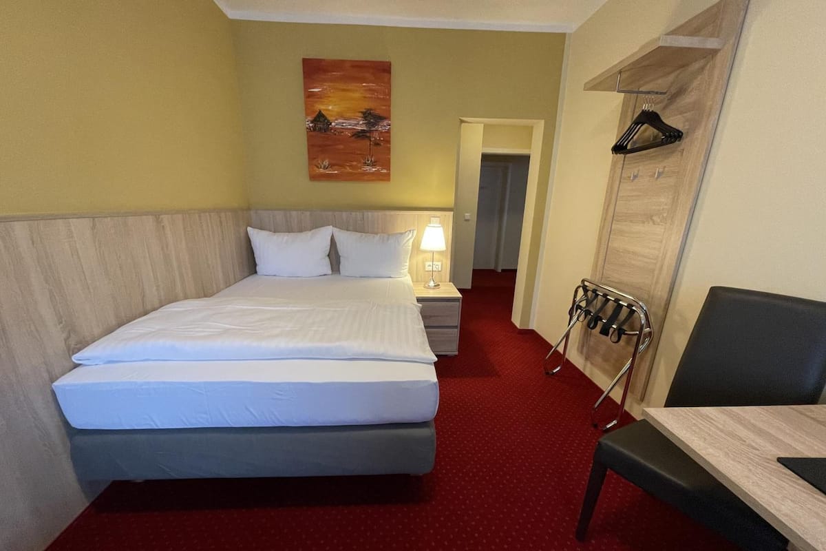 Une chambre d’hôtel comprenant un lit, une table de chevet, une lampe, une chaise et un porte-manteau.