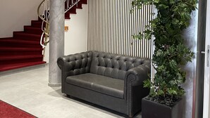 Un vestíbulo con alfombra roja, un sofá de cuero negro, una columna de mármol, una escalera con escalones rojos y una pared a rayas verticales.