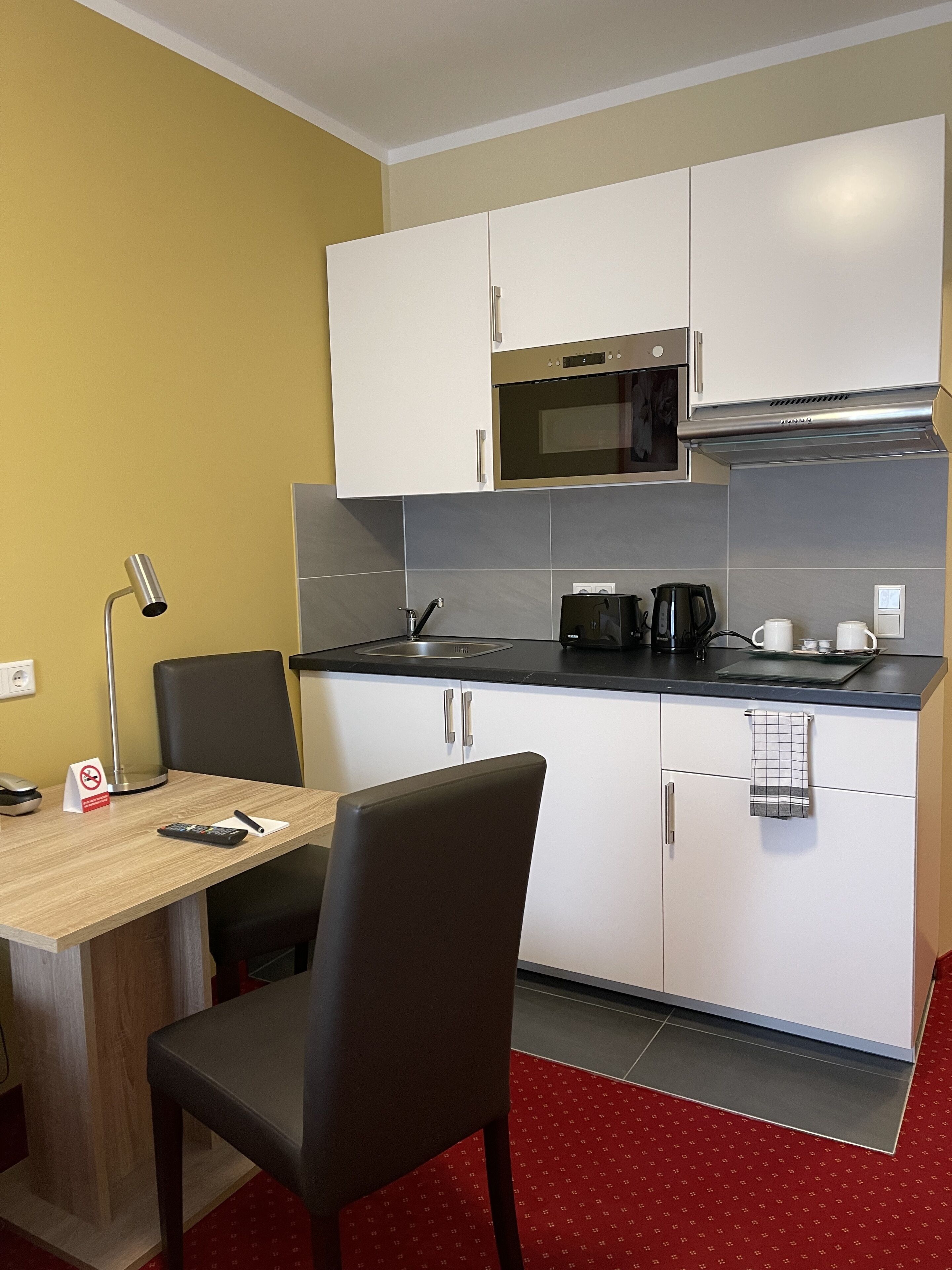 Cocina compacta con armarios blancos, microondas, cafetera y un pequeño comedor con mesa y sillas.