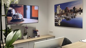 Un mostrador de recepción con un televisor de pantalla plana, una pintura de la ciudad y una orquídea en maceta.