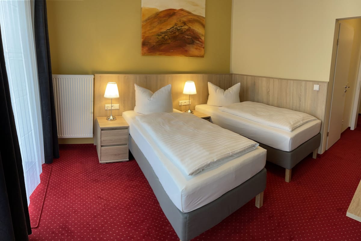 Une chambre d’hôtel avec deux lits, une moquette rouge, un tableau au mur et une porte.