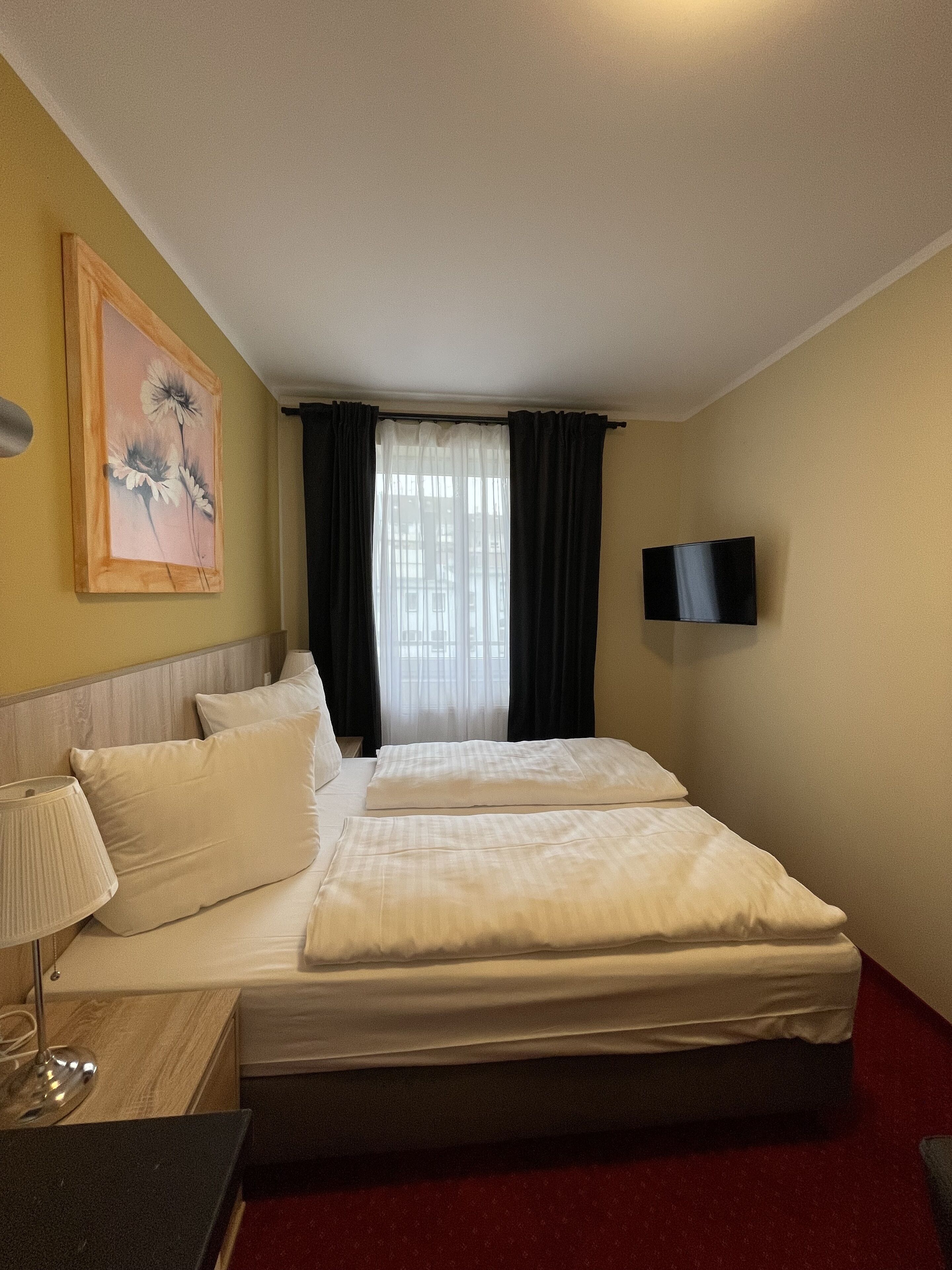 Habitación de hotel con dos camas, un televisor montado en la pared, un cuadro y una ventana con cortinas.