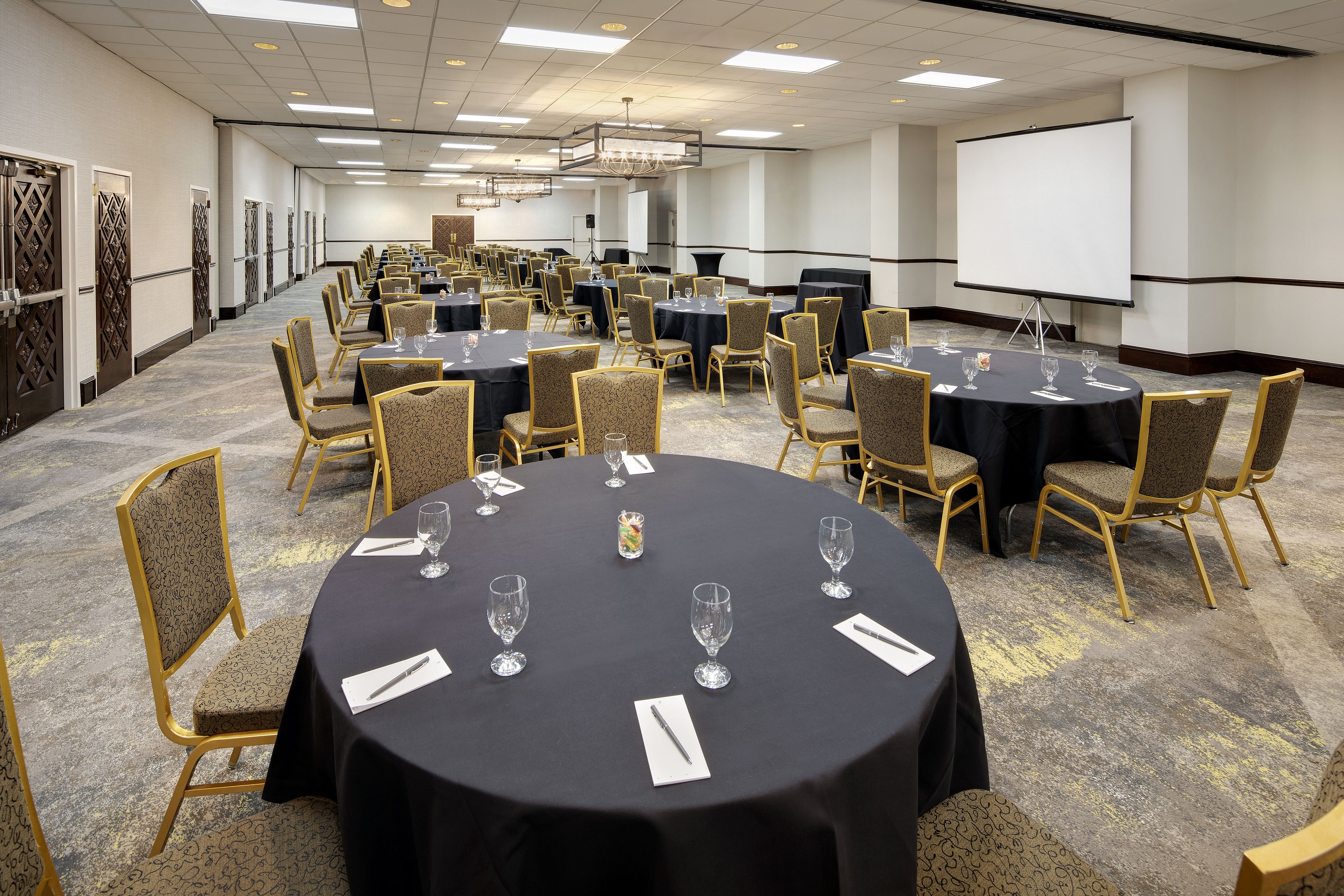 Une salle de conférence équipée de tables rondes, de chaises et d’un écran de projection.