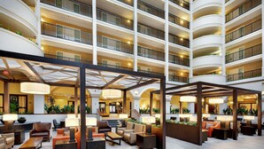 A multi-story hotel lobby with seating areas, a reception desk, and a staircase leading to upper floors.