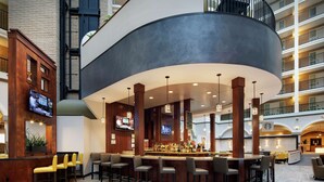A modern bar area with multiple seating options, including bar stools and high tables, surrounded by a curved ceiling structure.