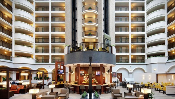 A spacious lobby with multiple seating areas, a central bar, and a high-ceiling atrium with balconies.