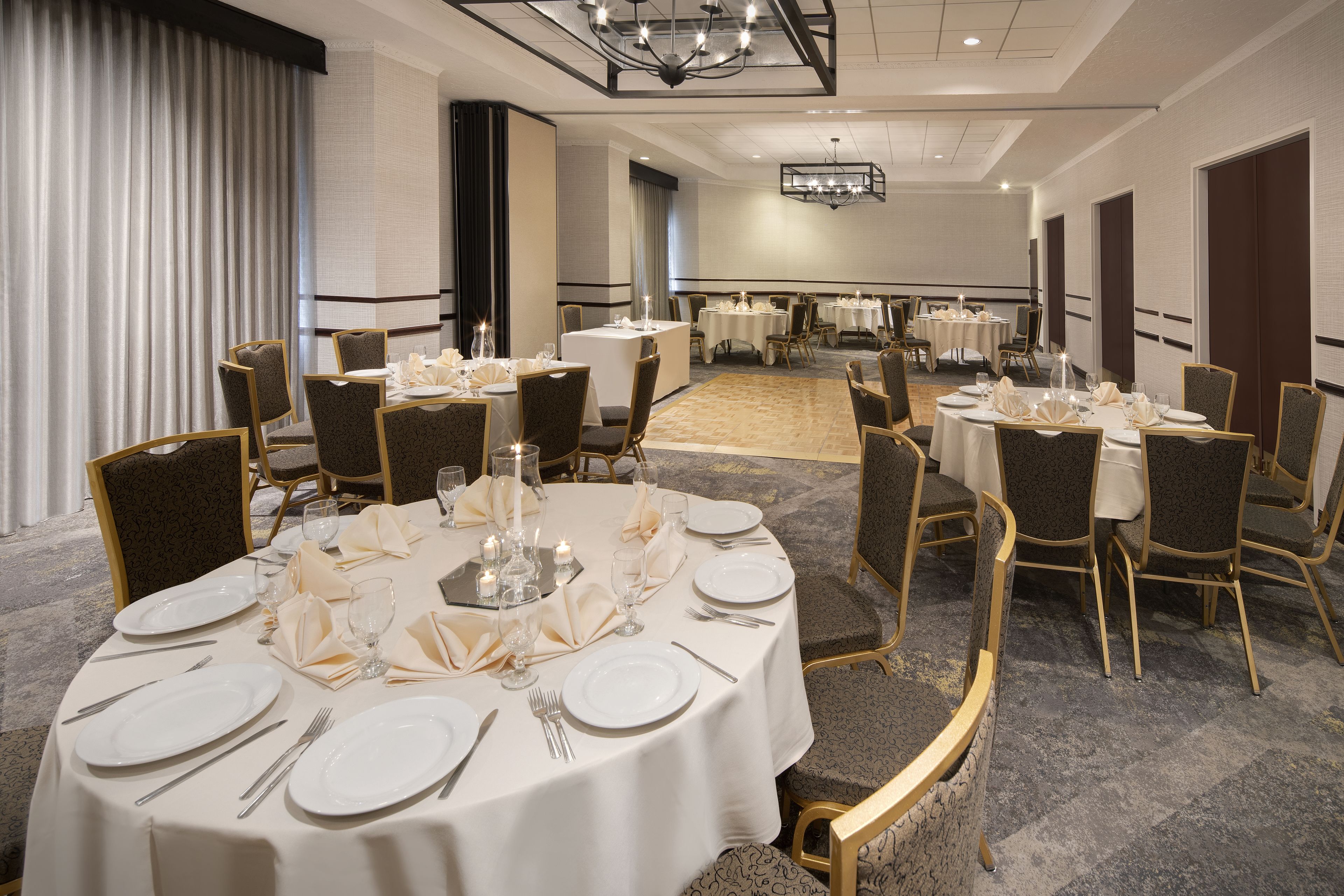 A banquet hall with round tables set for dining, featuring white tablecloths and gold chairs.