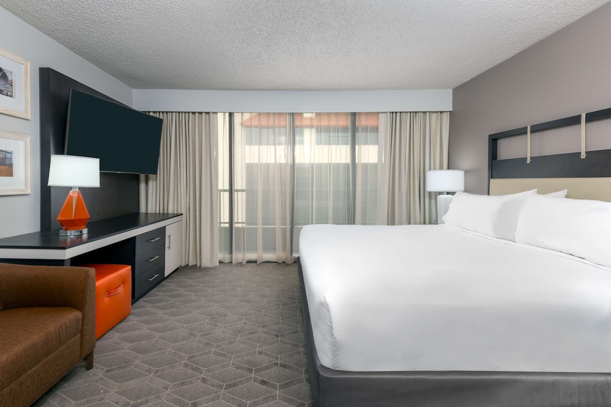 Una habitación de hotel con una cama, un escritorio con televisor, una silla y una ventana con cortinas.