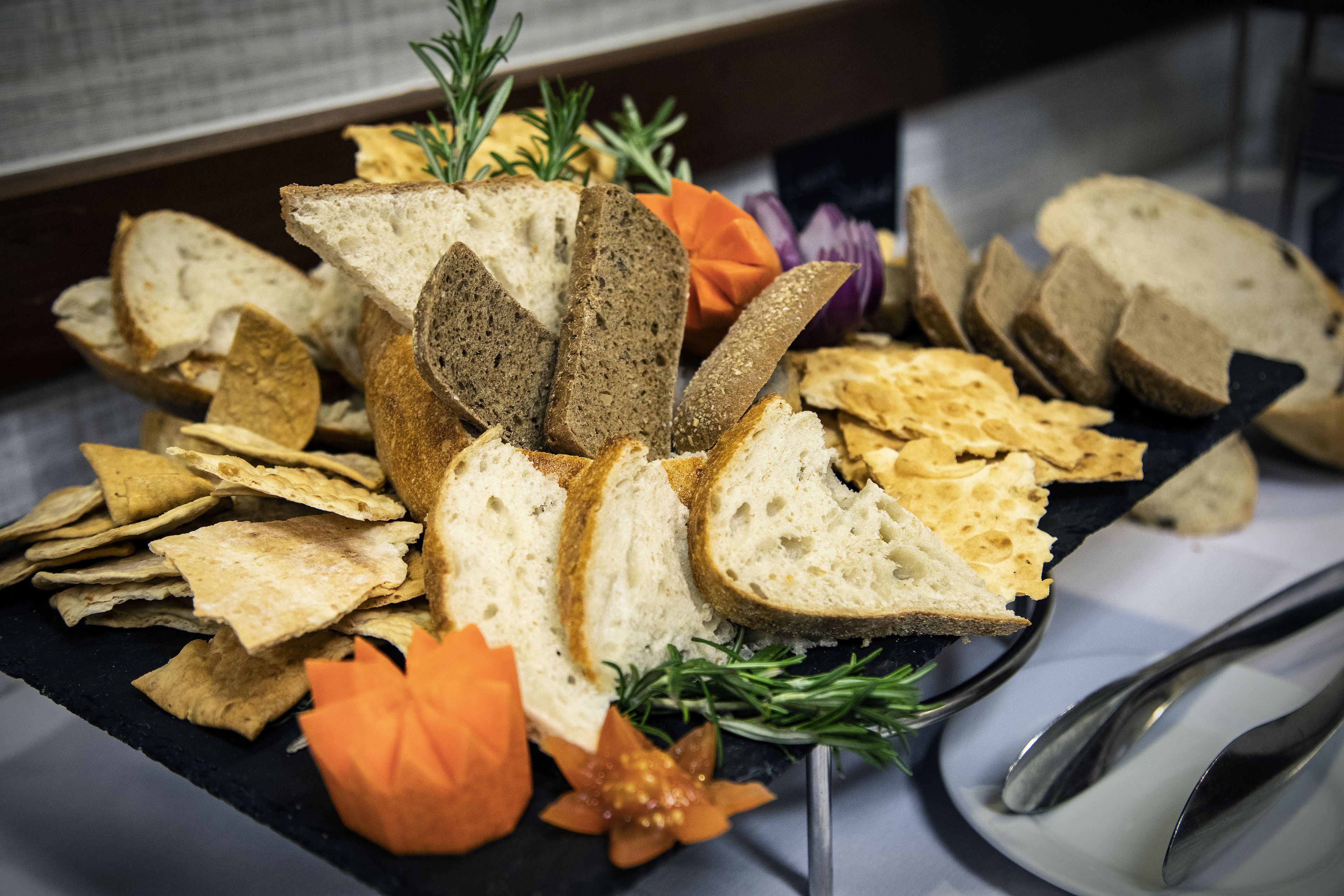 A variety of breads and crackers on a slate board, garnished with rosemary and other herbs.
