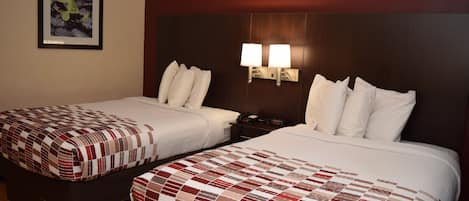 Dos camas individuales con ropa de cama a cuadros rojos y blancos, una mesita de noche con una lámpara y un cuadro en la pared.