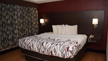 Een hotelkamer met een groot bed, twee bedlampen, een telefoon en een gordijn met een bloemendesign.