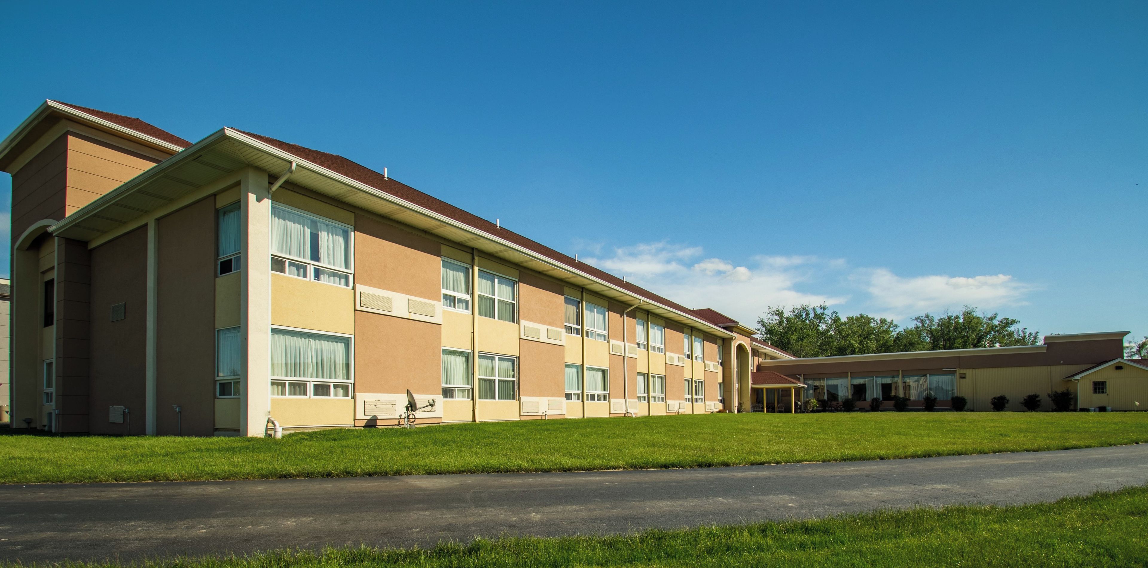 A multi-story building with a flat roof and large windows, surrounded by a well-maintained lawn and a paved road.
