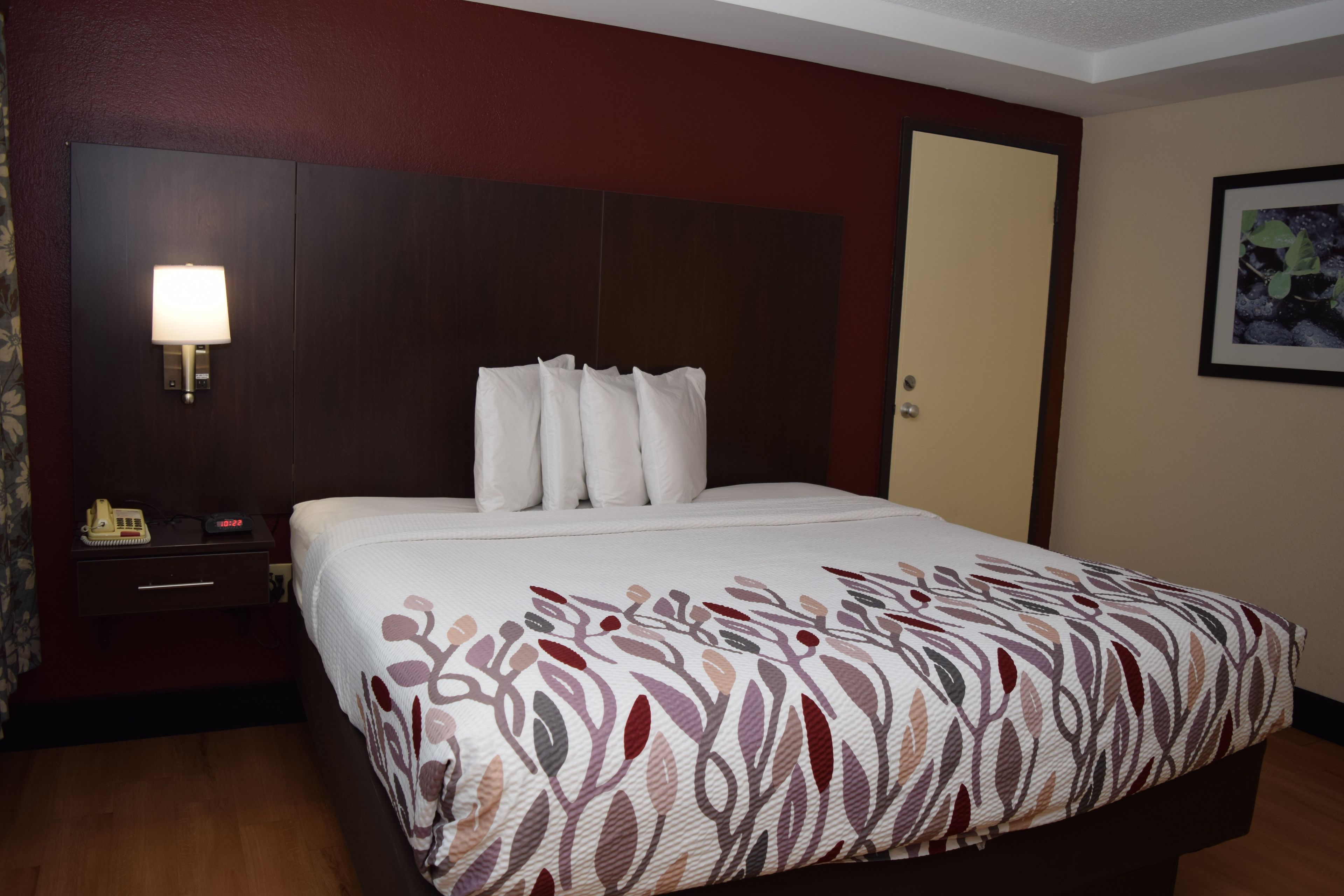 Una habitación de hotel con una cama, una mesita de noche, una lámpara y una puerta.