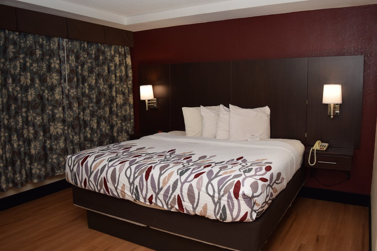 A hotel room with a large bed, two bedside lamps, a telephone, and a curtain with a floral pattern.