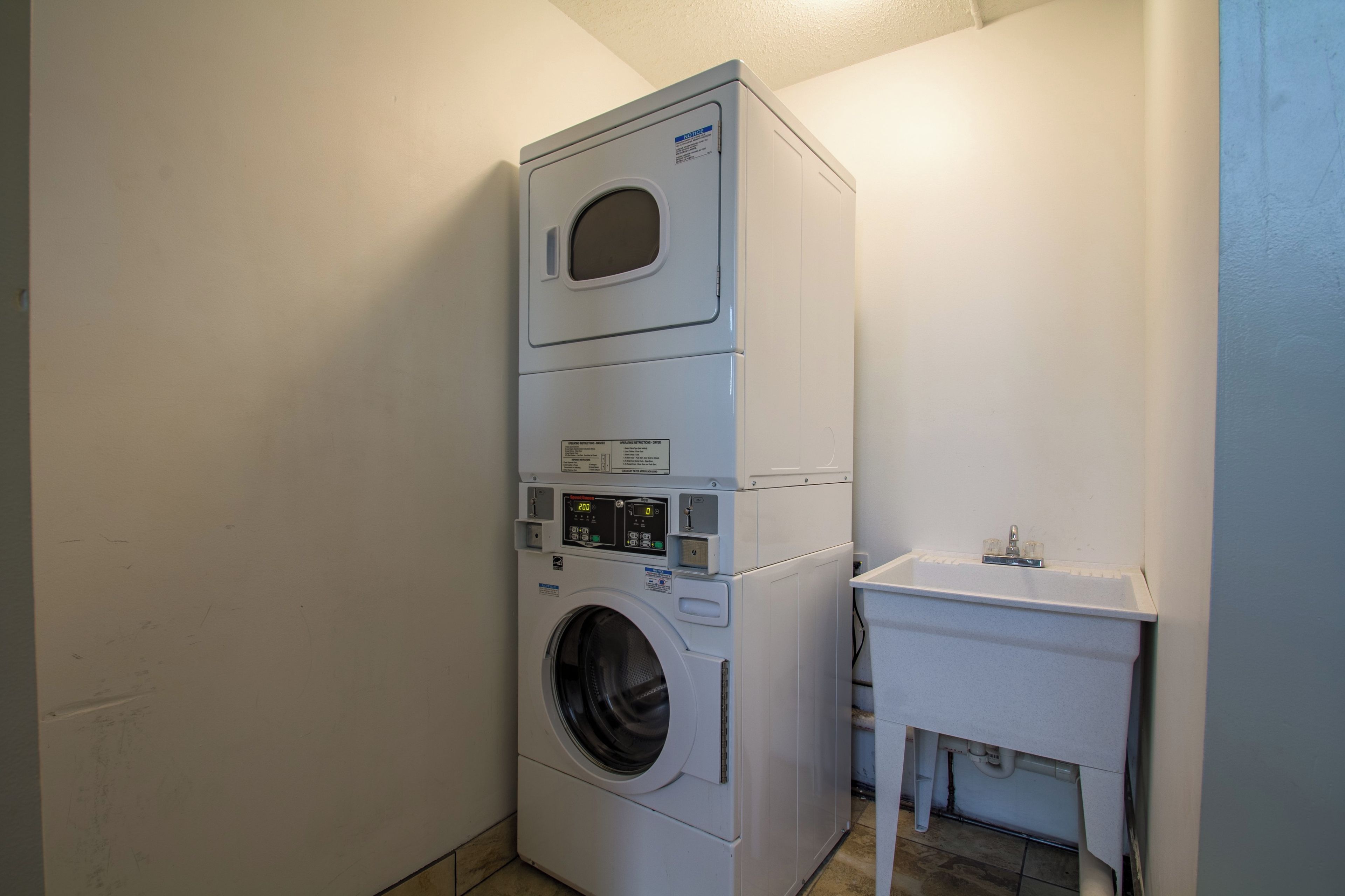 Una lavadora y secadora apiladas en un cuarto de lavado con un lavamanos pequeño y un armario.