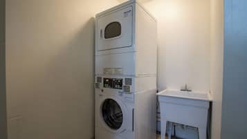 Una lavadora y secadora apiladas en un cuarto de lavado con un lavamanos pequeño y un armario.