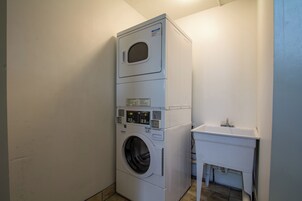 Una lavadora y secadora apiladas en un cuarto de lavado con un lavamanos pequeño y un armario.