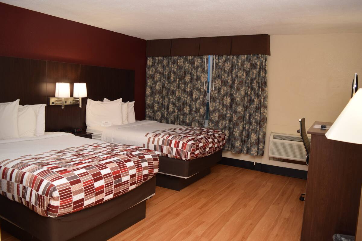 Une chambre d’hôtel avec deux lits, un plancher en bois, une grande fenêtre avec des rideaux et un bureau avec une lampe.