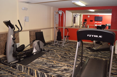 A fitness center with exercise equipment, including treadmills and a stationary bike, carpeted flooring, and a red accent wall.