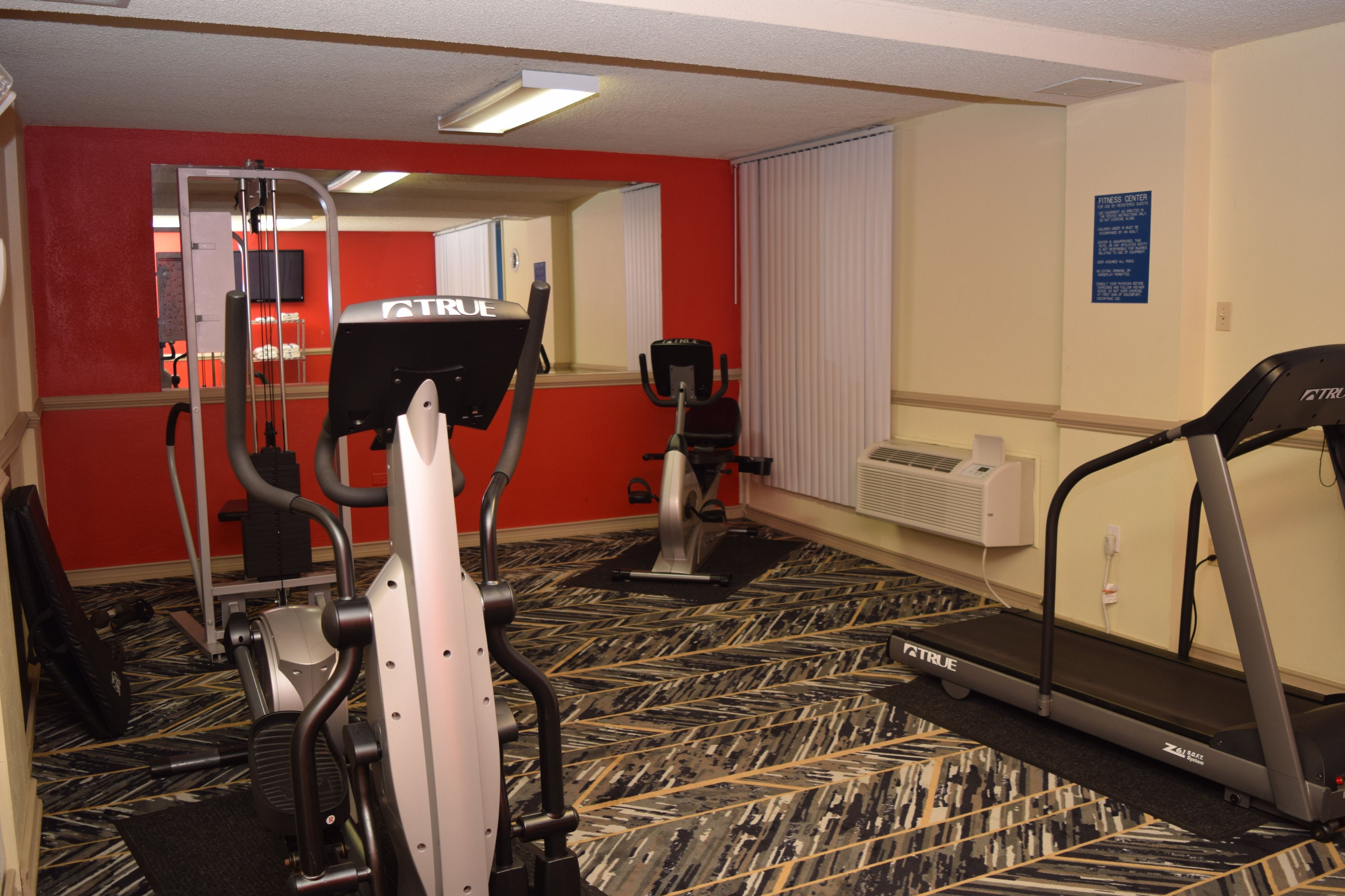 A fitness center with exercise equipment including a treadmill, elliptical, and weight machines.