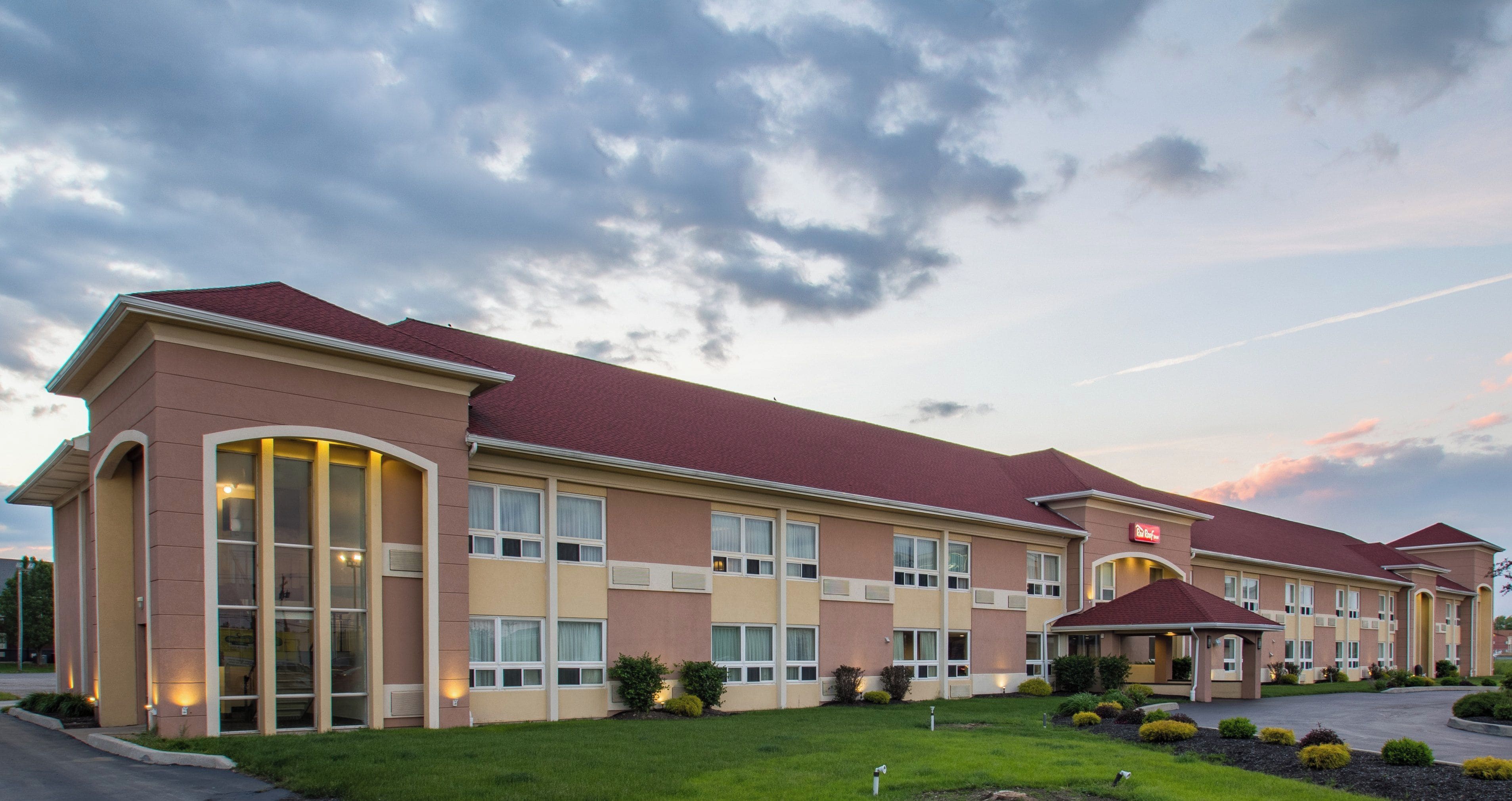 A hotel with a red roof, multiple windows, and a well-maintained lawn.