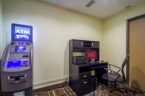 Una habitación de hotel con un cajero automático, un escritorio con una computadora y una silla.