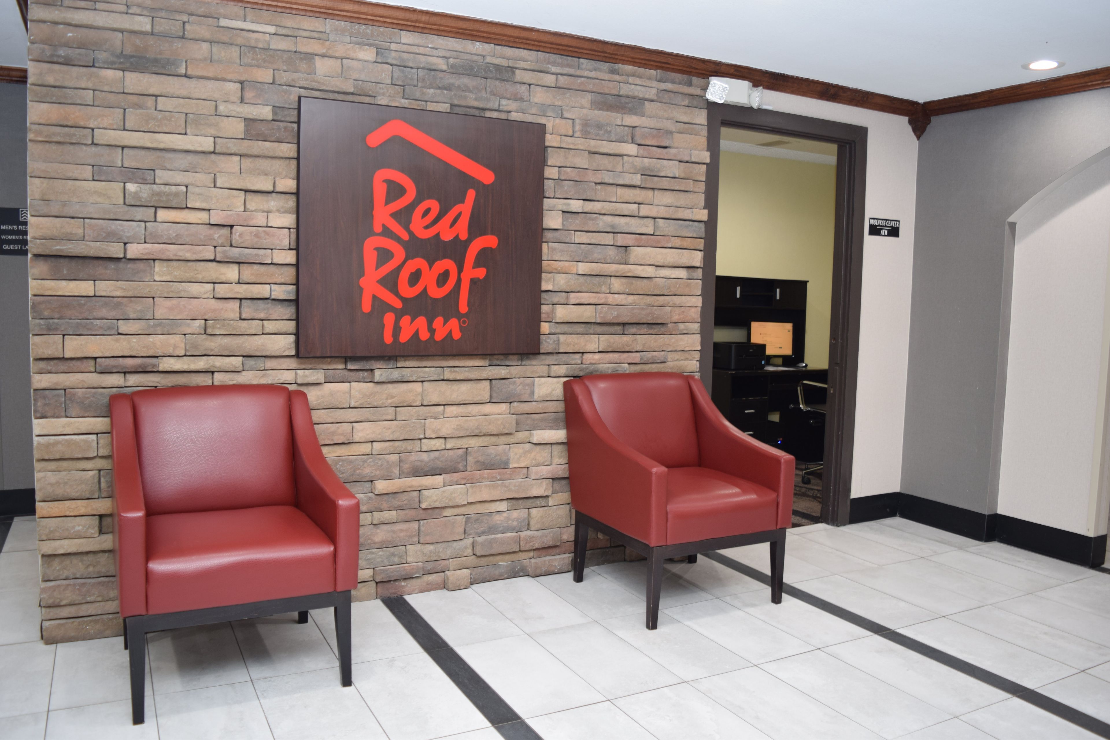 Een Red Roof Inn bord aan een bakstenen muur, twee rode leren stoelen en een bord met een business center.