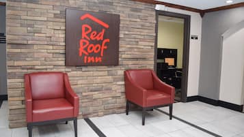 Een Red Roof Inn bord aan een bakstenen muur, twee rode leren stoelen en een bord met een business center.
