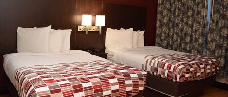 Habitación de hotel con dos camas, una mesita de noche, lámparas fijadas a la pared y cortina estampada con motivos florales.