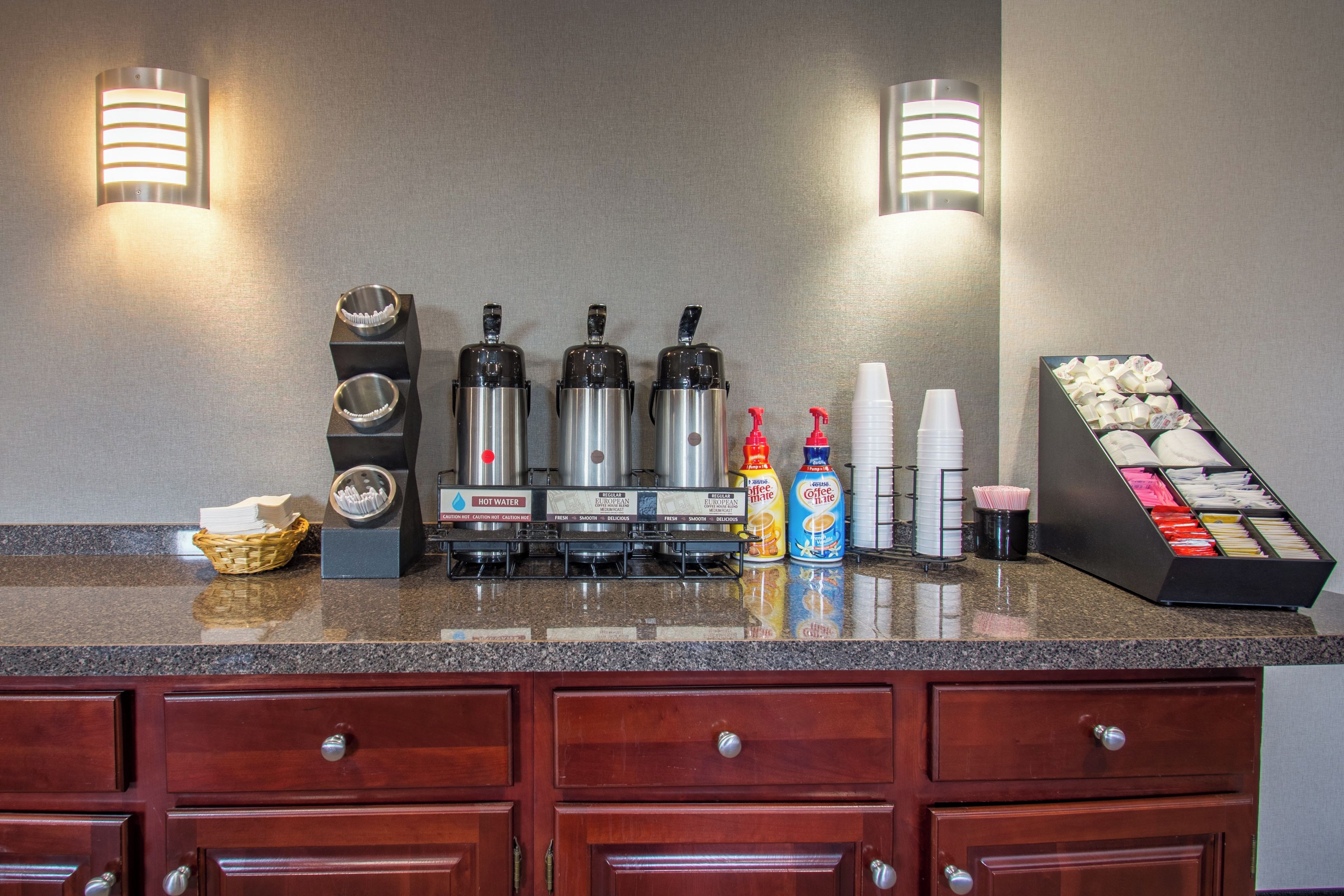 A hotel reception area with a coffee station, hot water dispensers, and a coffee machine.