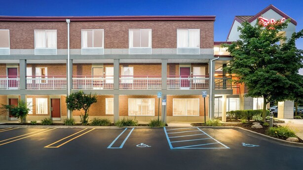A multi-story hotel with a brick facade, a parking lot with marked handicapped spaces, and a neon sign on the right. - HomeTowne Studios by Red Roof Auburn Hills (Auburn Hills)