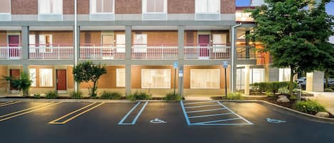 A multi-story hotel with a brick facade, a parking lot with marked handicapped spaces, and a neon sign on the right.