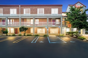 A multi-story hotel with a brick facade, a parking lot with marked handicapped spaces, and a neon sign on the right.