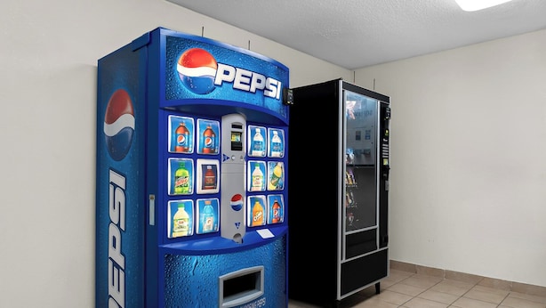 A blue Pepsi vending machine with various drink options and a black refrigerator next to it. - HomeTowne Studios by Red Roof Auburn Hills (Auburn Hills)