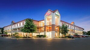 A hotel with a central tower, multiple balconies, and a parking lot. - HomeTowne Studios by Red Roof Auburn Hills (Auburn Hills)