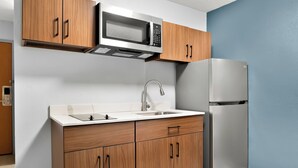 A kitchen with wooden cabinets, a stainless steel refrigerator, a microwave, and a sink. - HomeTowne Studios by Red Roof Auburn Hills (Auburn Hills)