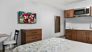 A bedroom with a bed, a chair, a dresser, a microwave, and a painting on the wall. - HomeTowne Studios by Red Roof Auburn Hills (Auburn Hills)