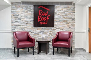 Zona de recepción de Red Roof Inn, con una pared de piedra y dos sillones de cuero rojo.