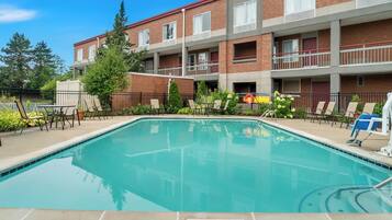 A rectangular pool with a 3-foot depth limit sign, surrounded by lounge chairs and a brick building with balconies.