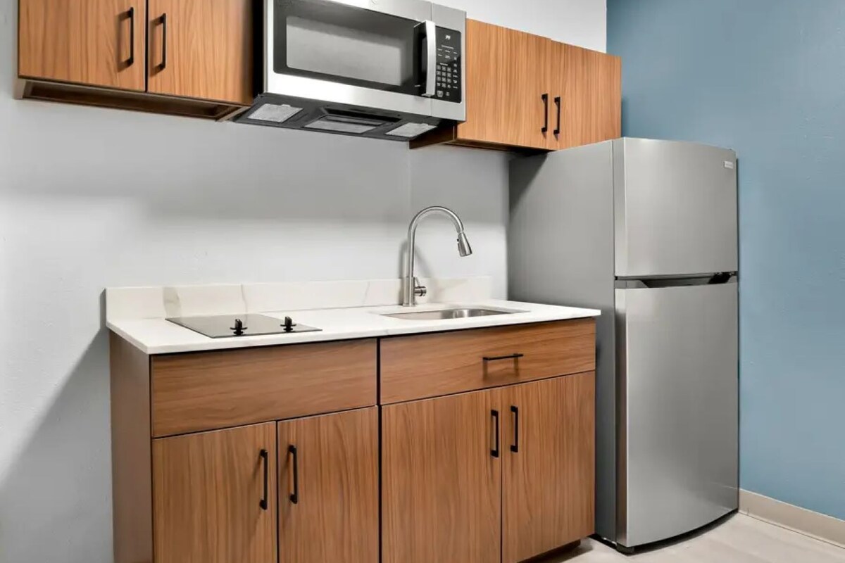 Una cocina con armarios de madera, un refrigerador de acero inoxidable, un microondas y un lavamanos.