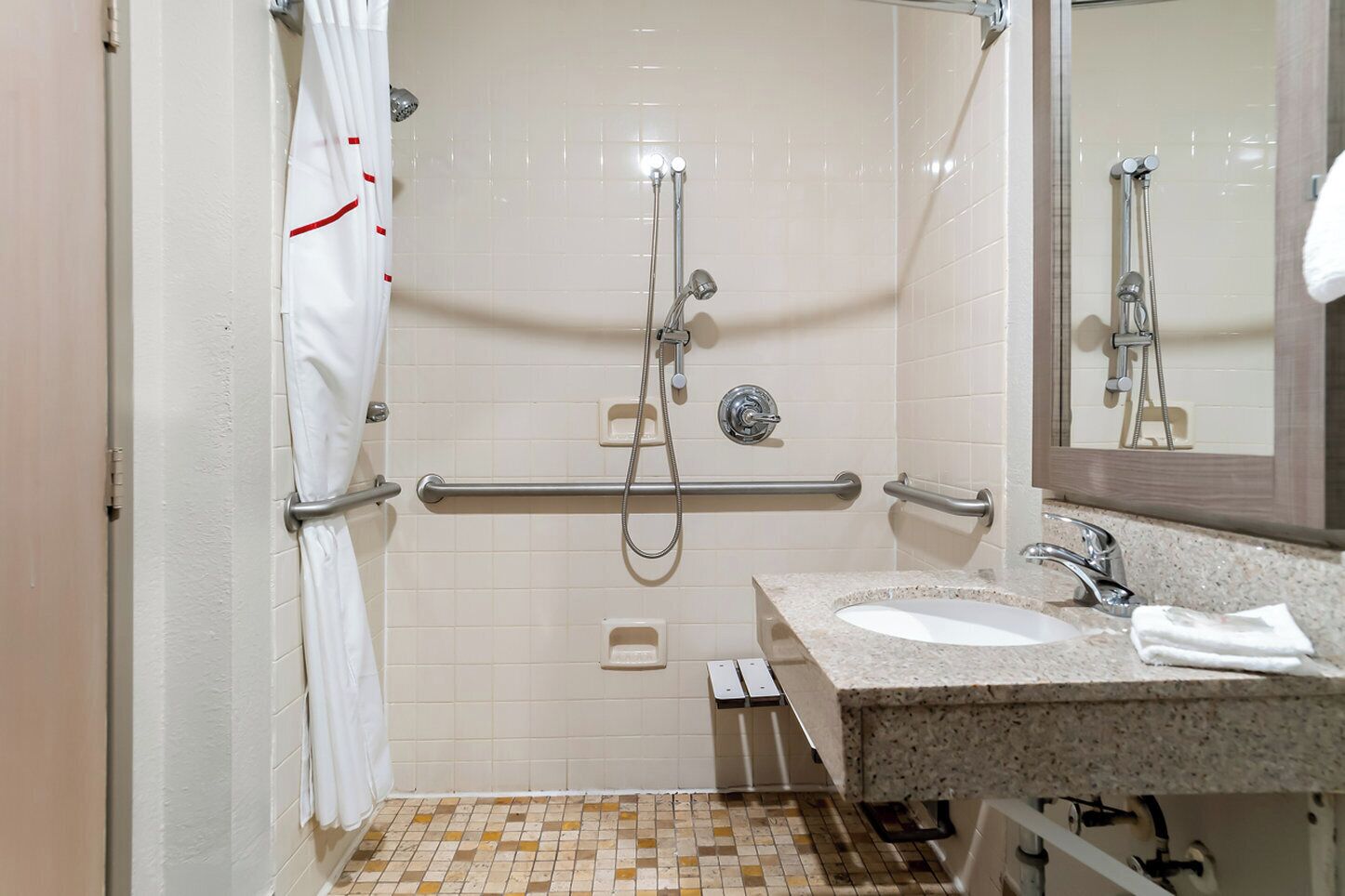 A bathroom with a shower, grab bars, a sink, and a mirror.